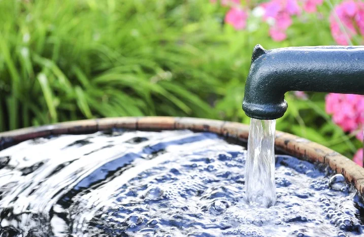 Wasser fließt aus einem grünen Wasserhahn in ein Holzfass.